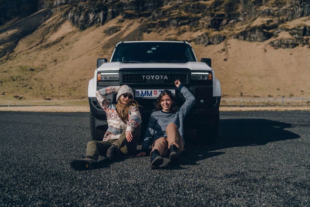 Two women sitting in front of a Toyota Land Cruiser in Iceland.