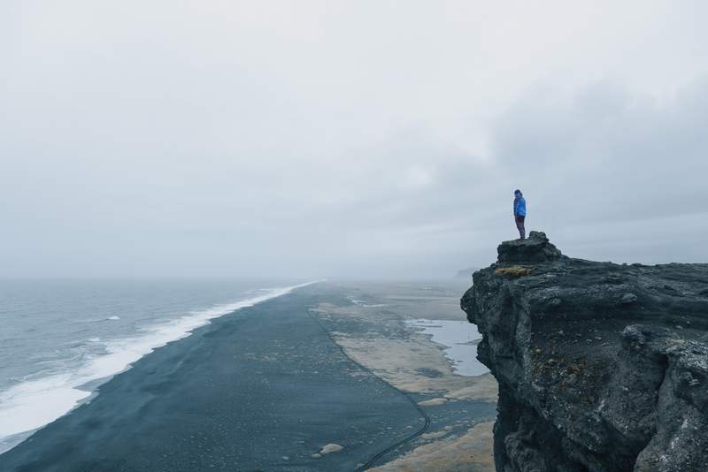 Man standing on cliff at black sand beach iceland