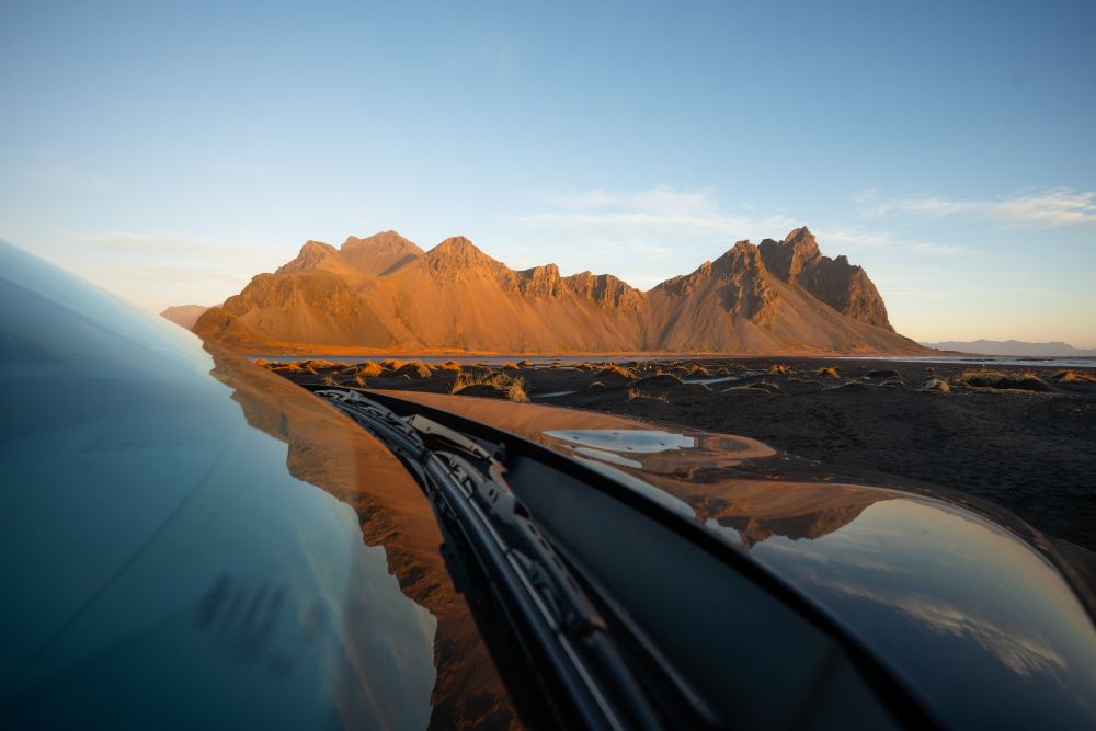 Car driving on the road in iceland with mountains in the background.